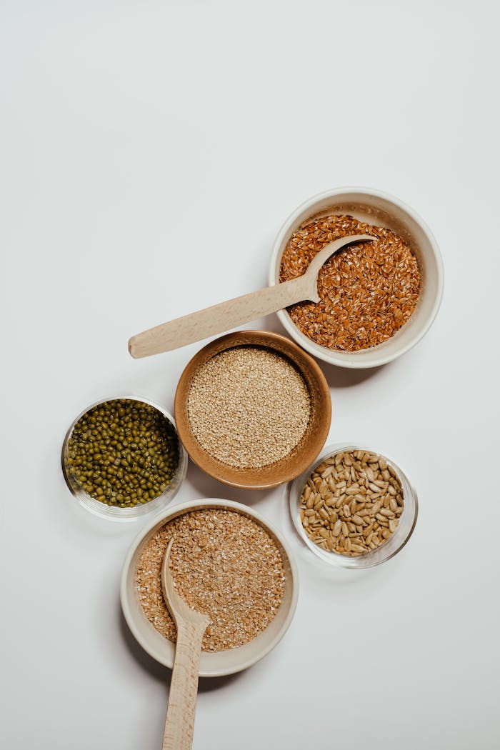 services-03 Top view of assorted grains in bowls with wooden spoons on a minimalist background.