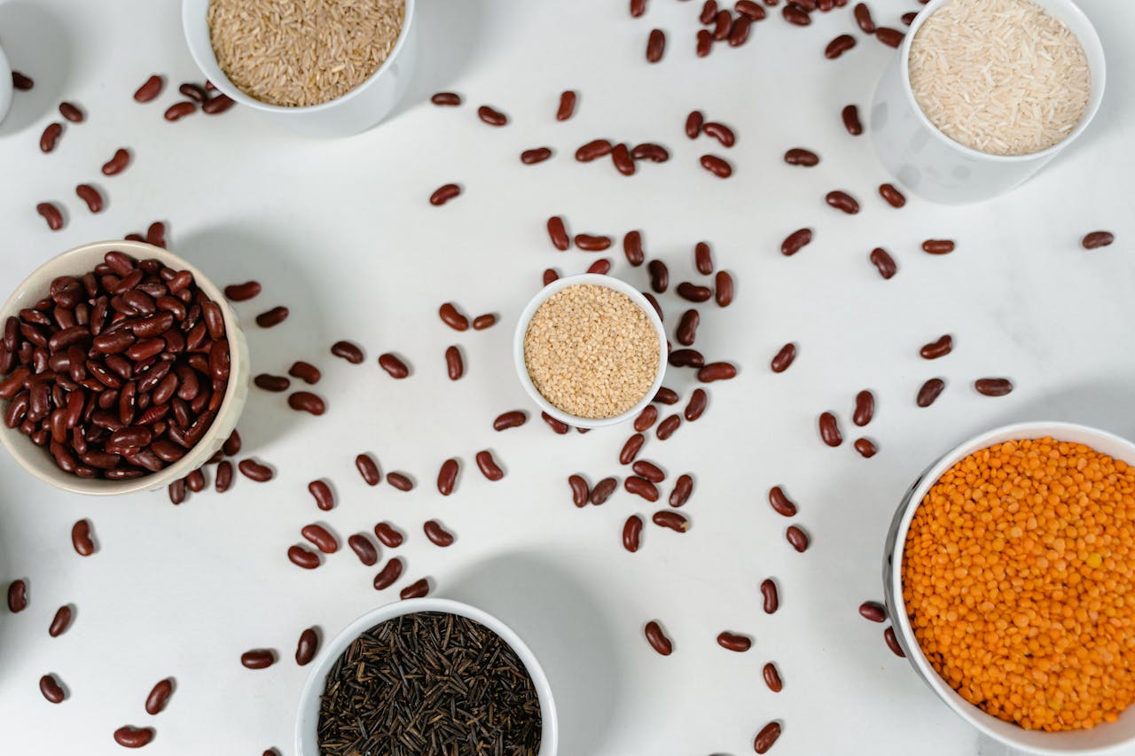 our-story Top view of various grains and pulses in bowls on a white surface.